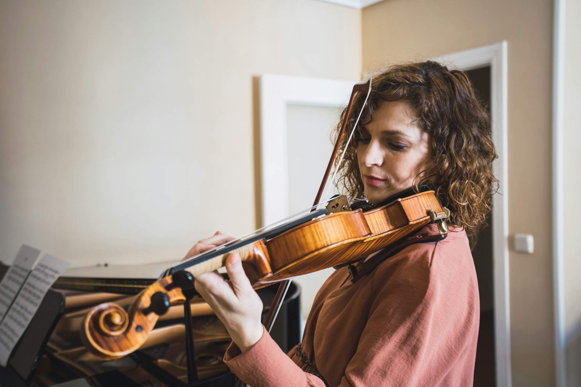 Pregnant woman playing on violin near piano in room