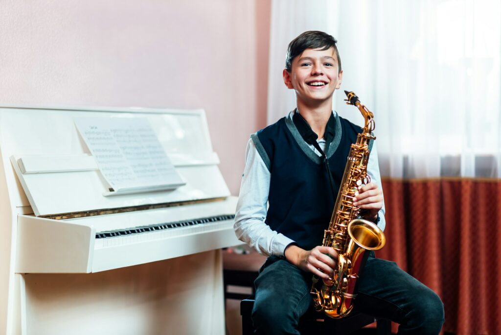 Cheerful student boy sitting with saxophone before music lesson