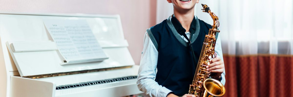 Cheerful student boy sitting with saxophone before music lesson